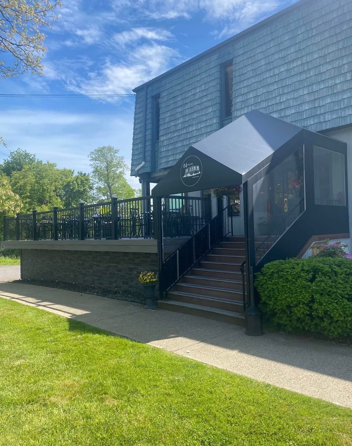 The Mansard Inn building set above Abbott Road — slate-shingle mansard roof, black awning, stone retaining wall, and staircase rising to the dining room