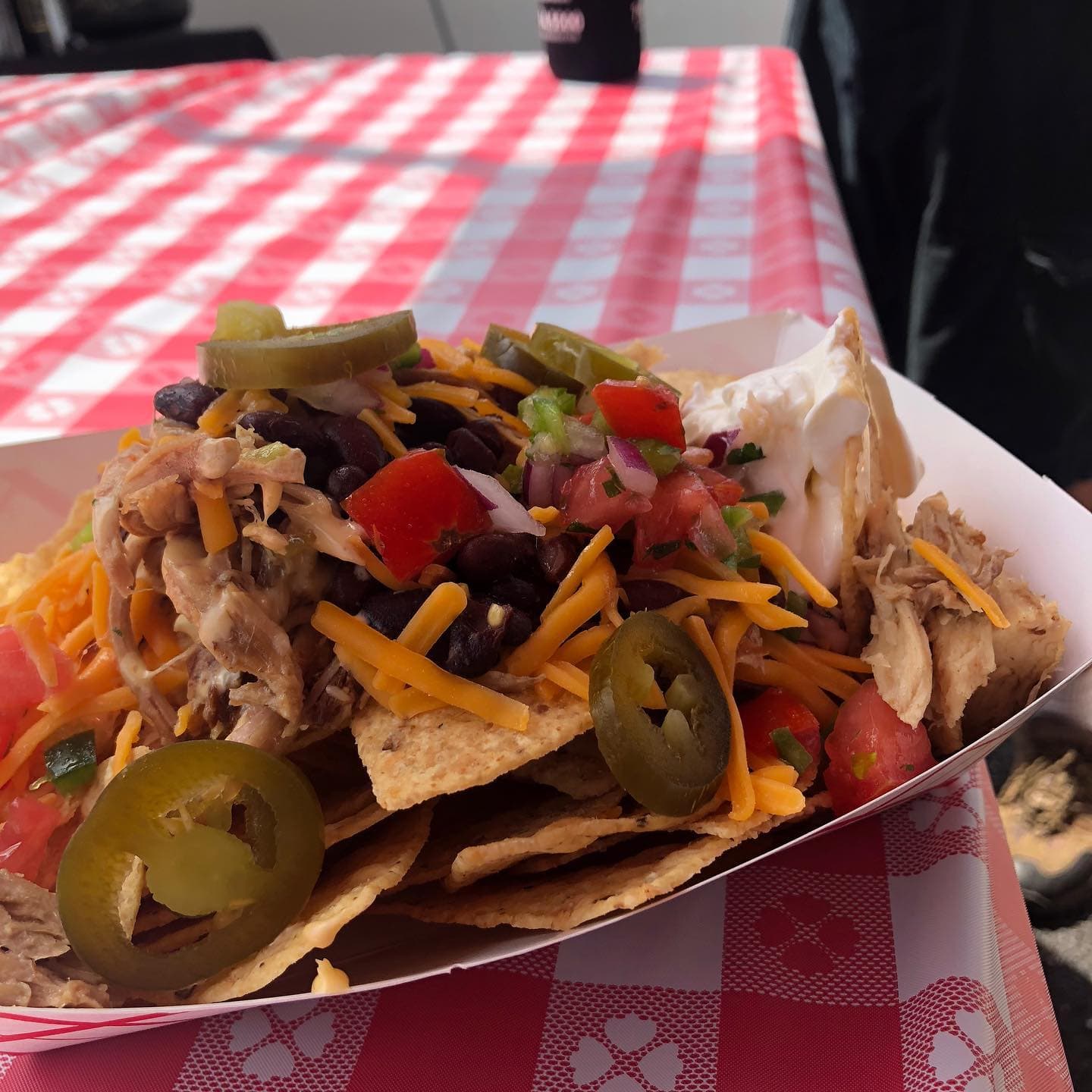 Loaded gameday nachos with pulled chicken, black beans, jalapeños, and cheddar on a red-checkered table